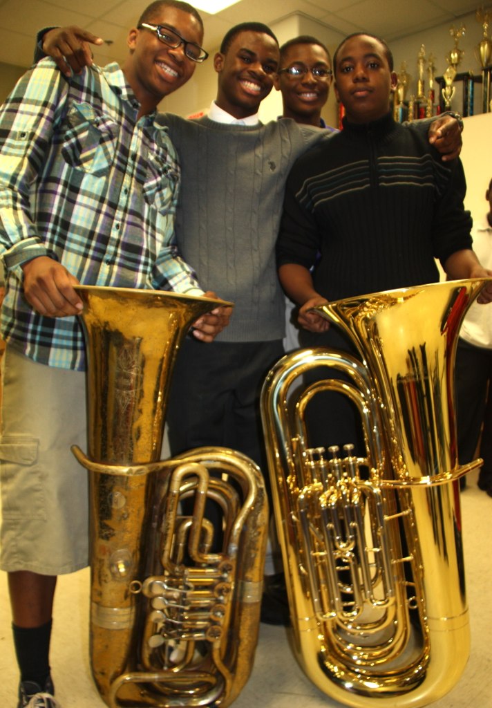 Four young black men gather smiling around two tubas.